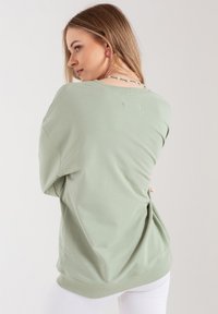 Jasnozielona, oversize'owa bluza z okrągłym dekoltem, ściągaczami na rękawach i luźnym krojem. Materiał wydaje się gładki, z minimalnymi detalami.