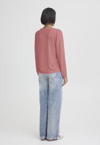 Langærmet, lyserød bluse med afslappet pasform og tekstureret stof. Kombineret med lyseblå højtaljede jeans med løs silhuet.