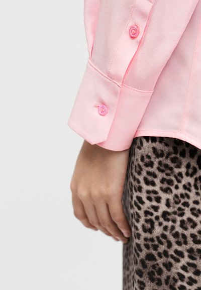 Ροζ σατέν πουκάμισο μακρυμάνικο με μανσέτες με κουμπιά, φορεμένο πάνω από μια φούστα με λεοπάρ σχέδιο. Απαλή υφή και εφαρμοστό σχέδιο με ζωηρό χρώμα.