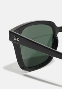 Čierne slnečné okuliare Ray-Ban s zelenými šošovkami, s hrubým rámom a detailom loga na spánku. Hladký povrch a ostrý dizajn.