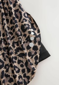 Tissu beige et noir à imprimé léopard avec quatre points ronds réfléchissants alignés verticalement sur le bord plié d'une manche noire.