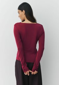 Dlhý rukáv marónová blúzka s širokým výstrihom a priliehavým strihom, s naťahovacími dlhými rukávmi a hladkou textúrou.