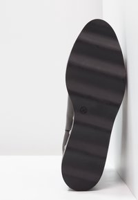 Suela de zapato negra con una textura suave, forma ligeramente redondeada y el tamaño indicado 36 moldeado en la parte inferior. Pared de fondo.