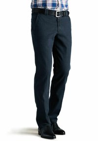 Jeans en denim bleu foncé avec une coupe droite, comportant des poches avant et une ceinture noire. Portés avec des bottes habillées noires.