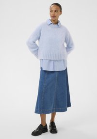 Pull bleu clair duveteux porté sur une chemise rayée bleu et blanc, associé à une longue jupe en denim et des chaussures noires.