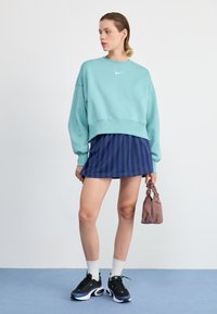 Light blue oversized sweatshirt with a white logo, paired with a navy striped skirt. Black sneakers, white socks, and a small brown bag.