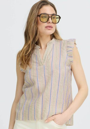 Kvinde iført briller med skildpaddemønster og gule linser samt en ærmeløs beige top med vertikale flerfarvede striber og flæseærmer.