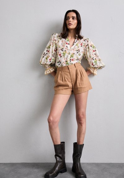 Blomstermønstrete bluse med lange ermer og puffermer, kombinert med beige høytlivsshorts og mørkebrune ankelboots.