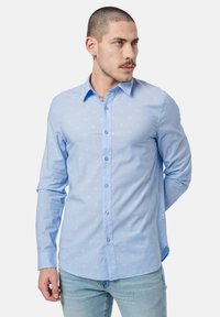 Camisa de botones azul claro hecha de una tela con un patrón sutil, con mangas largas, cuello y corte regular.