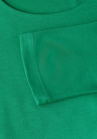 Vihreä puuvillakangas, jossa on pyöreä pääntie ja cuffitettu hiha, jolla on sileä pinta ja siistit saumat.