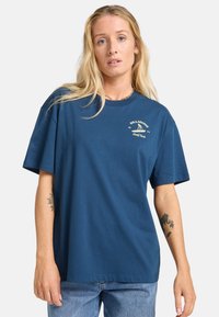 Marineblå bomulds T-shirt med korte ærmer, rund halsudskæring og et grafisk logo i cremefarve på venstre bryst. Casual fit.