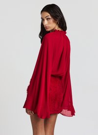 Robe en chiffon rouge avec un col froncé, des manches de cape fluides et une jupe texturée à motif de roses. L'ourlet est froncé.