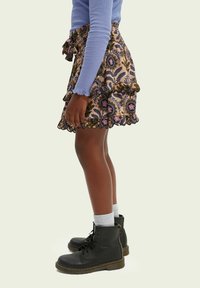 Brun mønstret nederdel med flæser og bølget kant, kombineret med sorte snørestøvler og hvide sokker, båret med en blå langærmet top.