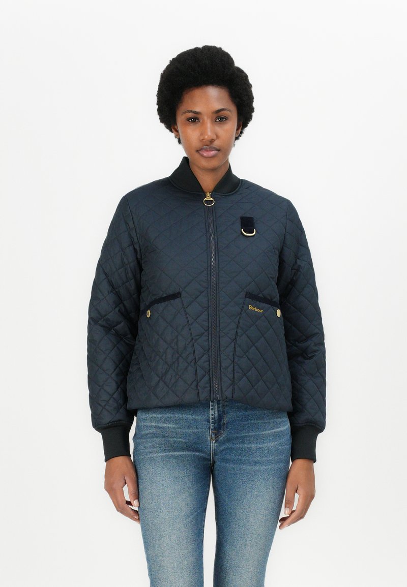 Navy quilted bomber jacket with a ribbed collar, zip closure, and two front pockets. Features a gold logo and a fabric accent on the chest.