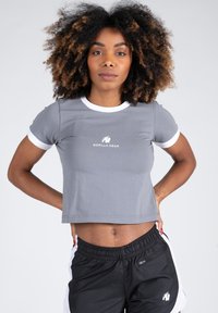 Grijze crop top met witte accenten en een logo, gemaakt van rekbaar materiaal. Heeft korte mouwen en een getailleerd ontwerp.