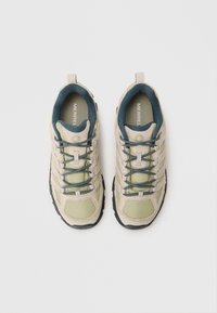 Pair of beige and olive green Merrell hiking shoes with black and white laces viewed from above on white background.