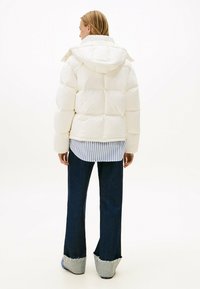 Chaqueta blanca de plumas con capucha, con diseño acolchado, combinada con una camisa a rayas y unos vaqueros acampanados azules con detalles de tela gris en los dobladillos.