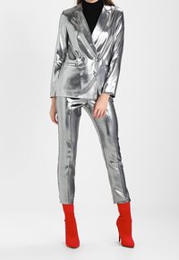 Metalický stříbrný oblek se dvouřadým sakem a slim fit kalhotami, doplněný jasně červenými kotníkovými botami. Hladký, lesklý povrch.
