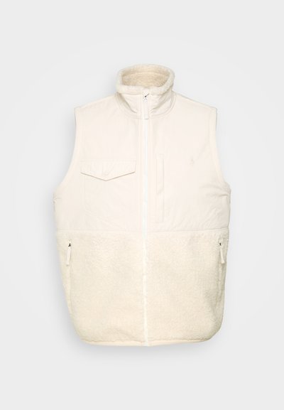 Colete sem mangas forrado com tecido tipo lã na cor branco sujo. Apresenta proteção para o queixo, fecho de correr frontal, bolso no peito e dois bolsos laterais com fecho de correr.