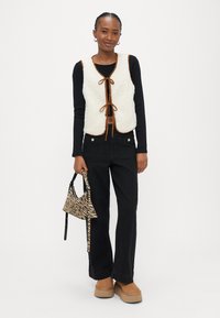 Hvit vest i falsk pels med brun kant og bånd, svart langermet topp, svarte vide jeans, brune platåsko og en veske med zebrastriber.