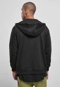 Sudadera negra con capucha ajustable, puños de canalé y dobladillo en capas, confeccionada en una tela suave que destaca por su textura lisa.