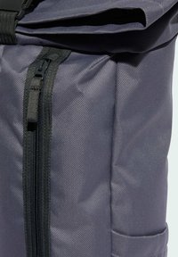 Šedý látkový batoh s texturovaným povrchem, horním víkem, černým zipem a boční kapsou. Jednoduchý, funkční design pro každodenní použití.