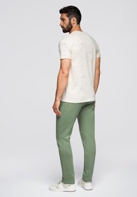 Heren crème t-shirt met een gestructureerd, gespetterd patroon, gecombineerd met groene joggerbroeken en witte sneakers. Eenvoudige en casual outfit.