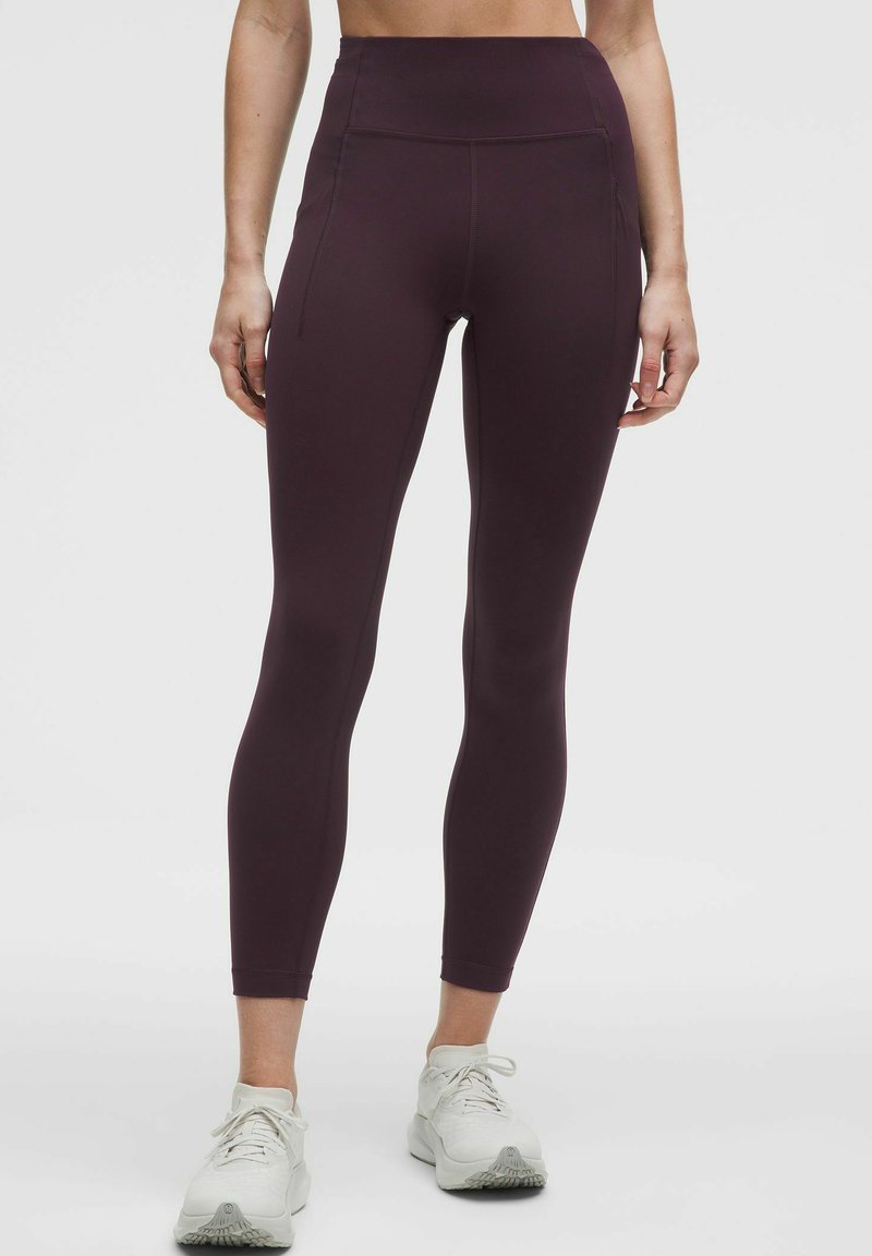 Bordeče visokokakovostne legice iz elastičnega materiala z gladko teksturo in ravnimi šivi, v kombinaciji z belimi športnimi čevlji.