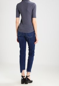 Harmaa ribbineulottu lyhythihainen pusero yhdistetty tummansinisiin slim fit -farkkuihin, joissa on rispaantuneet reunat, ja mustiin korkokenkiin. Yksinkertainen muotoilu, istuva siluetti.