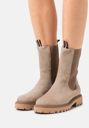 Beige Wildleder-Stiefeletten mit elastischen Seitenteilen, strukturierten Oberflächen und klobigen Gummisohlen. Verfügen über gestreifte Laschen zum einfachen An- und Ausziehen.
