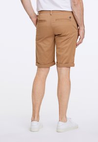 Ruske puuvillashortsit, joissa on kääntöhelma, kaksi takataskua ja logotunnus vyötäröllä, käytettynä valkoisten tennareiden kanssa.