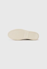 Shoe sole in beige rubber with a textured pattern and rectangular logo accent. Smooth surface with a rounded toe design.