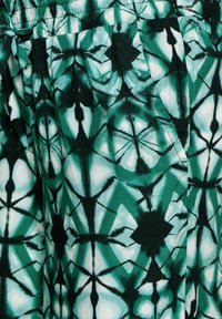 Vihreässä kuviollisessa kankaassa on geometrinen muotoilu, jossa tummanvihreät ja valkoiset muodot ja viivat vaihtelevat, luoden tekstuurimaisen ulkonäön.