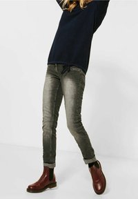 Marinblått texturkappa med dragsko i nederkant, parat med grå slim-fit jeans och burgundy ankle boots med elastiska sidopaneler.