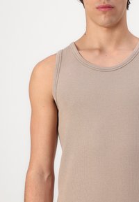 Beige puuvillainen hihaton paita ribbikuvioinnilla, pyöreällä pääntiellä ja hihattomalla designilla, esittäen tiukkaa siluettia.
