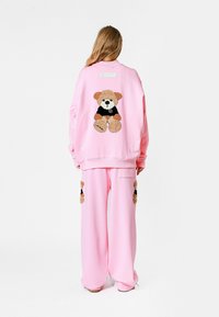 Conjunto de sudadera y pantalones en color rosa con un diseño de oso de peluche en la parte trasera. Material suave, corte holgado, con acentos bordados destacados en las piernas.