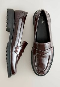 Loafers en cuir verni bordeaux avec une semelle en caoutchouc noir, dotés d'une sangle à l'avant et de détails texturés sur le dessus.