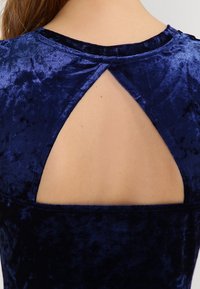 Navy niebieska sukienka z weluru z detalem w kształcie dziurki z tyłu. Gładka tekstura i swobodny fason. Okrągły dekolt i krótkie rękawy.