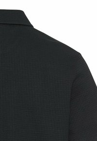 Sort tekstureret polo shirt med et ribbet mønster og en klassisk krave. Stoffet fremstår let og åndbart.
