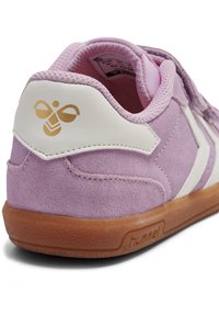 Różowy zamszowy sneaker z białymi akcentami i gumową podeszwą w kolorze naturalnym, z złotym logo pszczoły na pięcie. Cholewka o fakturze oraz wyściełany kołnierz.