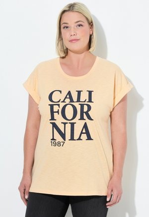 Persikkavärinen t-paita, jossa on pyöreä kaula-aukko ja käännetyt lyhyet hihat. T-paidassa on suuri tummansininen printti, jossa lukee "CALIFORNIA 1987."