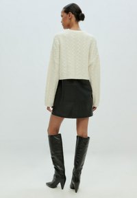 Creme kabelgebreide trui, cropped design; zwarte leren mini-rok; hoge zwarte haklaarzen; gladde texturen en contrasterende kleuren.