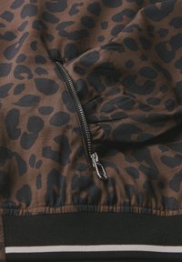 Hnědá zipová bunda s černým leopardím vzorem. Mezi její funkce patří zipová kapsa a černý pruhovaný lem, s hladkou texturou.