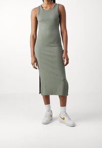 Ribbad, ärmlös, olivgrön midiklänning med sidoklyfta, i kombination med vita sneakers och vita strumpor. Enkel, figurnära design.