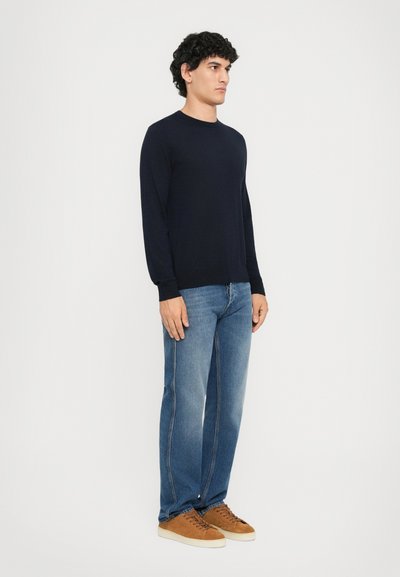 Marineblauer langärmliger Pullover kombiniert mit hellblauen gerade geschnittenen Jeans und braunen Schnürsneakern. Glatte Textur und lässiges Design.