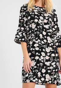 Černé květinové šaty s krátkými rozšířenými rukávy, jemnými vzory růžových a bílých květin a volným střihem pro snadnost pohybu.