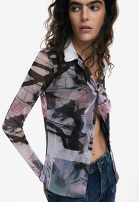 Long-sleeve shirt featuring a sheer, patterned fabric in shades of black, pink, and blue, with a white collar and button detailing.