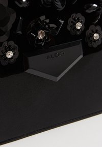 Czarna torebka z teksturowanymi kwiatowymi zdobieniami i kryształowymi akcentami. Logo ALDO wytłoczone na matowej, czarnej plakietce z metalu.