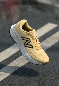 Yellow running shoe with breathable mesh upper, black accents, padded collar, and lightweight sole, displayed floating above a textured surface.