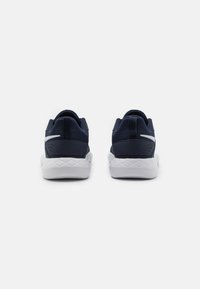 Chaussures de sport bleu marine foncées avec un dessus en maille texturée, semelle blanche et accents réfléchissants. Comprend un col rembourré et un design de talon distinctif.